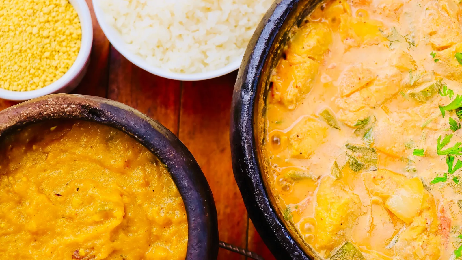 A traditional Brazilian moqueca and side dishes served in clay pots on a wooden table